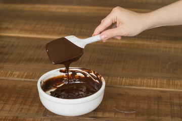 Poster - Shot of melted chocolate dripping from a cake shovel into a white ceramic bowl on a wooden table