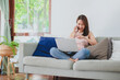 © interstid - Beautiful Asian woman smiling while working at home via laptop notebook and mobile phone in living room