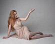 © faestock - Full length portrait of pretty red haired woman dancer,  wearing skin toned flowing fairy dress. Sitting gestural poses  isolated on studio background.