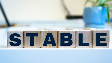 Poster - STABLE is a word written in black letters on wooden cubes.