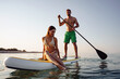 © fotofabrika - Couple of tourists young man and woman having fun paddleboarding at sea