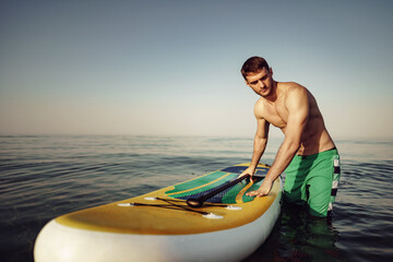 Wall Mural - Young fit man on paddle board floating on lake.