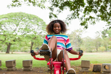 Wall Mural - Cute African American girl with curly hair playing at the playground in the park.