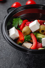 Wall Mural - Delicious Greek salad with tomatoes, olives and fresh herbs, a fresh salad on the menu of a fast food restaurant on a dark stone table. Healthy option of fast food.