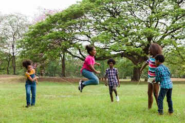 group of african american children having fun jumping over the rope in the park. cheerful kid jumpin