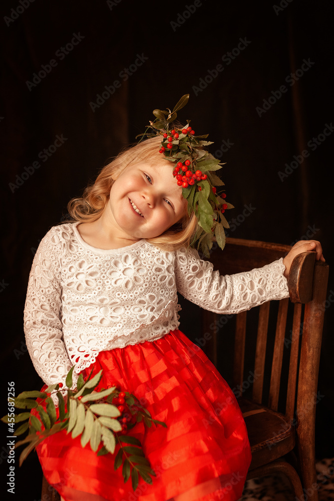 little girl. girl is sitting on chair in red dress with a wreath ...