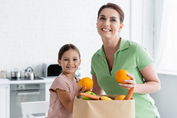 Wall Mural - Happy mother and kid standing near paper bag with food in kitchen