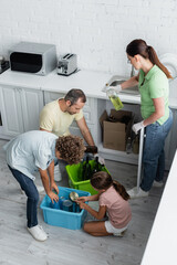 Wall Mural - Kids sorting trash near parents in kitchen