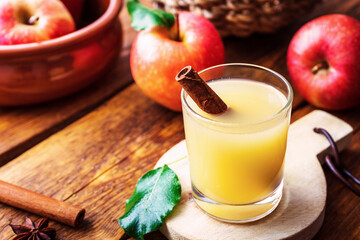 Heißer Apfelwein in einem Glas mit Zimtstange und rote Äpfel auf einem braunen Holz Tisch. Rustikaler Stil, Herbst.