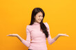 © Chanakon - Attractive Beautiful asian woman open hands palm up holding something. Surprised happy female on isolated yellow background. Thai teenage girl around 20.