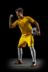 Full-length portrait of male professional football player after winning match isolated over black background