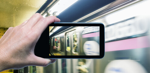 Wall Mural - Female hand with smartphone taking a picture of New York subway train. Tourism concept