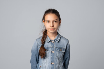 Portrait of smiling preteen girl looking at camera with happy facial expression, isolated on grey background, wearing in denim jacket