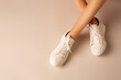 White sneakers shoes and girl’s legs on nude background - casual footwear