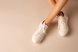 Fototapeta  - White sneakers shoes and girl’s legs on nude background - casual footwear
