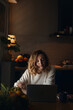 © Pietro Karras/Stocksy - Woman using laptop in dark kitchen
