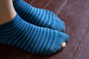 Wall Mural - female legs in striped blue torn socks on the old wooden red floor, torn socks on the girl's legs, feet