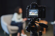 © LIGHTFIELD STUDIOS - digital camera with curly african american journalist talking with businessman in suit during talk show on screen