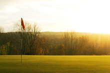 Golf Flag And Green With Warm Yellow Sun Rays In Autumn