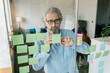 © Mihajlo Ckovric/Stocksy - Businessman writing notes on a stickers on a glass wall