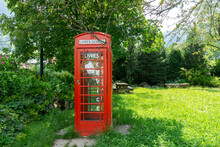 Red British Phone Booth With An Idea To Share Books In Public Place. Relaxing Park.