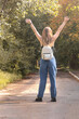 © Ольга Рязанцева - A young girl with a white backpack stands in full growth outdoors, two hands are raised up.