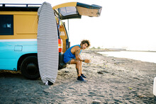 Traveler With Surfboard Resting Near Van On Beach