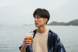 © Heng Yu/Stocksy - Asian man drinking a beverage by the seaside