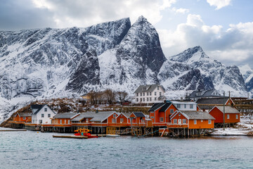 Wall Mural - Lofoten islands, Norway, fishing village with red rorbu huts on the coast, snowy mountains in the background.