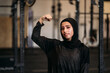© Manu Padilla/Stocksy - Smiling fit Muslim sportswoman showing biceps in gym