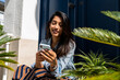 © Alba Vitta/Stocksy - Smiley young woman looking at phone sitting outdoors