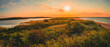 Beautiful painting-like sunrise seascape over South Cape Beach on Cape Cod. The sun rising over the green sand dunes and horizon.