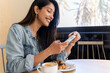 © Alba Vitta/Stocksy - Happy young woman looking at phone in cafeteria