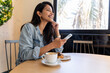 © Alba Vitta/Stocksy - Happy young woman looking at phone in cafeteria