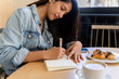© Alba Vitta/Stocksy - Young woman writing notes while coffe break