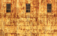 Rusty, Corrugated Metal Panels On A Yellow And Brown Building Surrounds Rusted Windows. 
