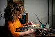 © Albert Martinez/Stocksy - Side view of a woman lampworker working with glass tubes and torch in her workshop