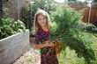 © Maria Manco/Stocksy - Little girl holds fresh harvested carrots from vegetable garden in her backyard