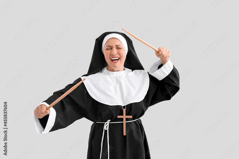 Mature nun with drum sticks on light background