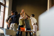 © KOTO - Casual business people raising hands in circle in sunny office meeting