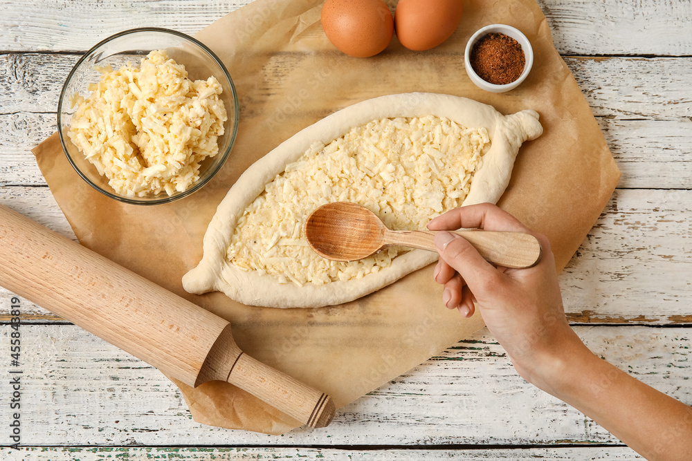 Woman preparing Ajarian khachapuri on light wooden background