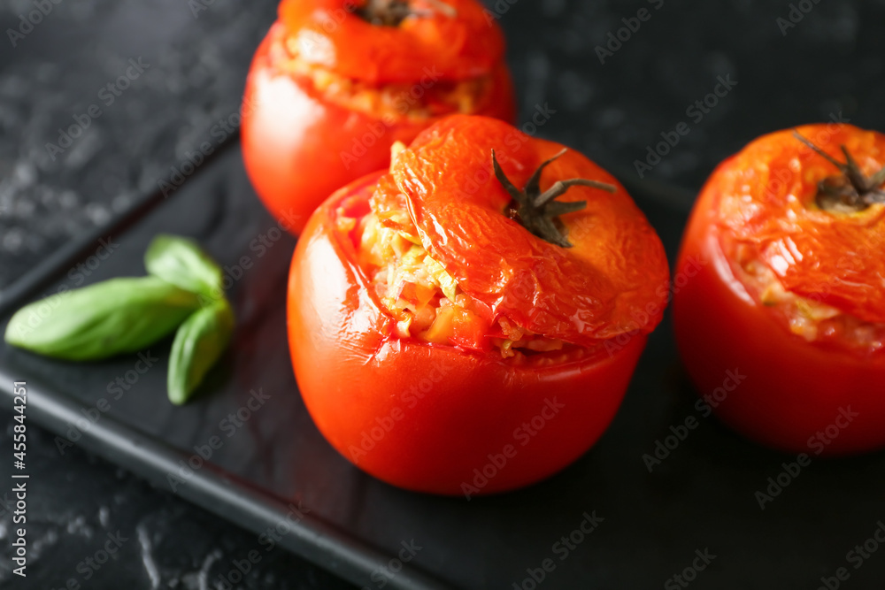 Board with tasty stuffed tomatoes on dark background, closeup