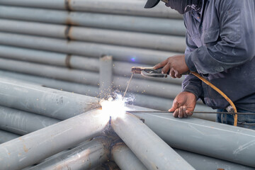 Worker welding pole structure outdoor with spark in car park.