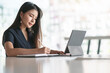 © NAMPIX - Young asian woman writing on notebook with pencil while working with laptop and paperwork at office desk.