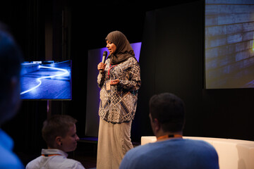 Wall Mural - Female speaker in hijab on stage talking to audience