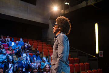 Audience watching male speaker with arms outstretched on stage