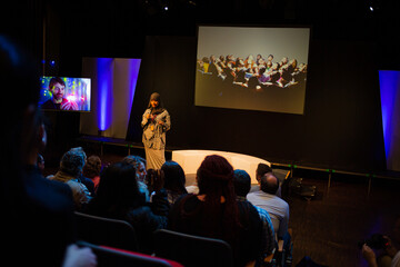 Smiling female speaker in hijab talking with microphone on stage