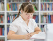 Young girl with down syndrome doing homework at library. Education for disabled children concept