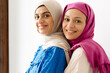 Two middle eastern women in headscarf hugging and smiling at camera