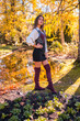 © unai - Autumn lifestyle, a young Caucasian brunette, in a black skirt and maroon boots with a seductive look, in a park by a lake